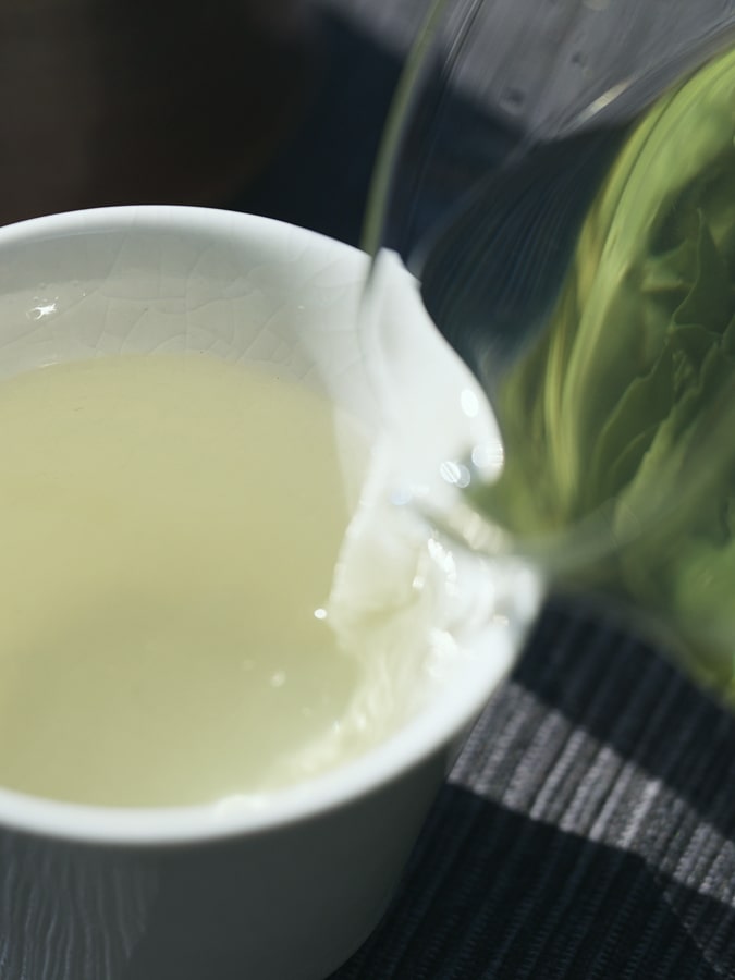 Pouring beautiful pale green tea into a tea vessel